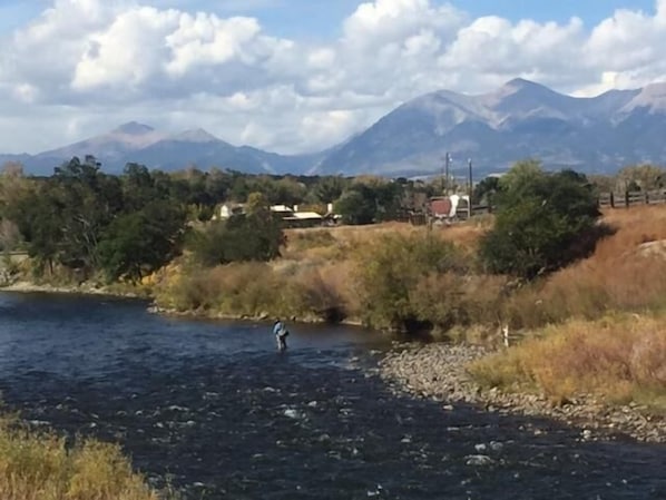 A river with a person fishing, surrounded by mountains and sparse vegetation.