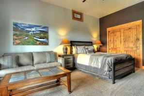 A bedroom with a bed, a sofa, a coffee table, and a painting on the wall.
