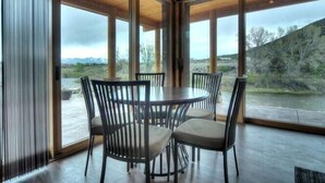A dining area with a round table and chairs, large windows, and a view of a river and hills. - River Time 1 Bedroom Holiday Home By Pinon Vacation Rentals (Salida)
