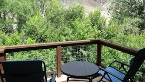 A deck with a table and chairs, overlooking a forested area and hills.