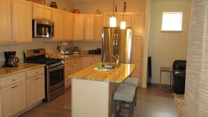 A modern kitchen with wooden cabinets, stainless steel appliances, a central island with stools, and pendant lighting.