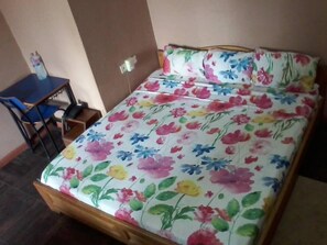 A bed with a floral bedspread, a wooden headboard, and a small table with a chair beside it. - Samartine Hotel (Kwabenya)