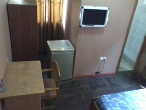 A small room with a bed, a desk, a chair, a small table, a television, and a washing machine. - Samartine Hotel (Kwabenya)