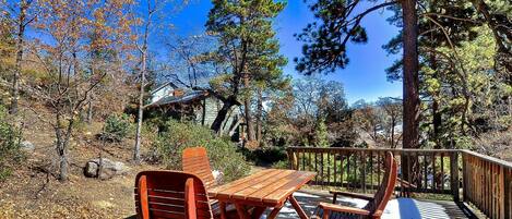 A wooden deck with a picnic table and chairs, surrounded by trees and a house in the background.