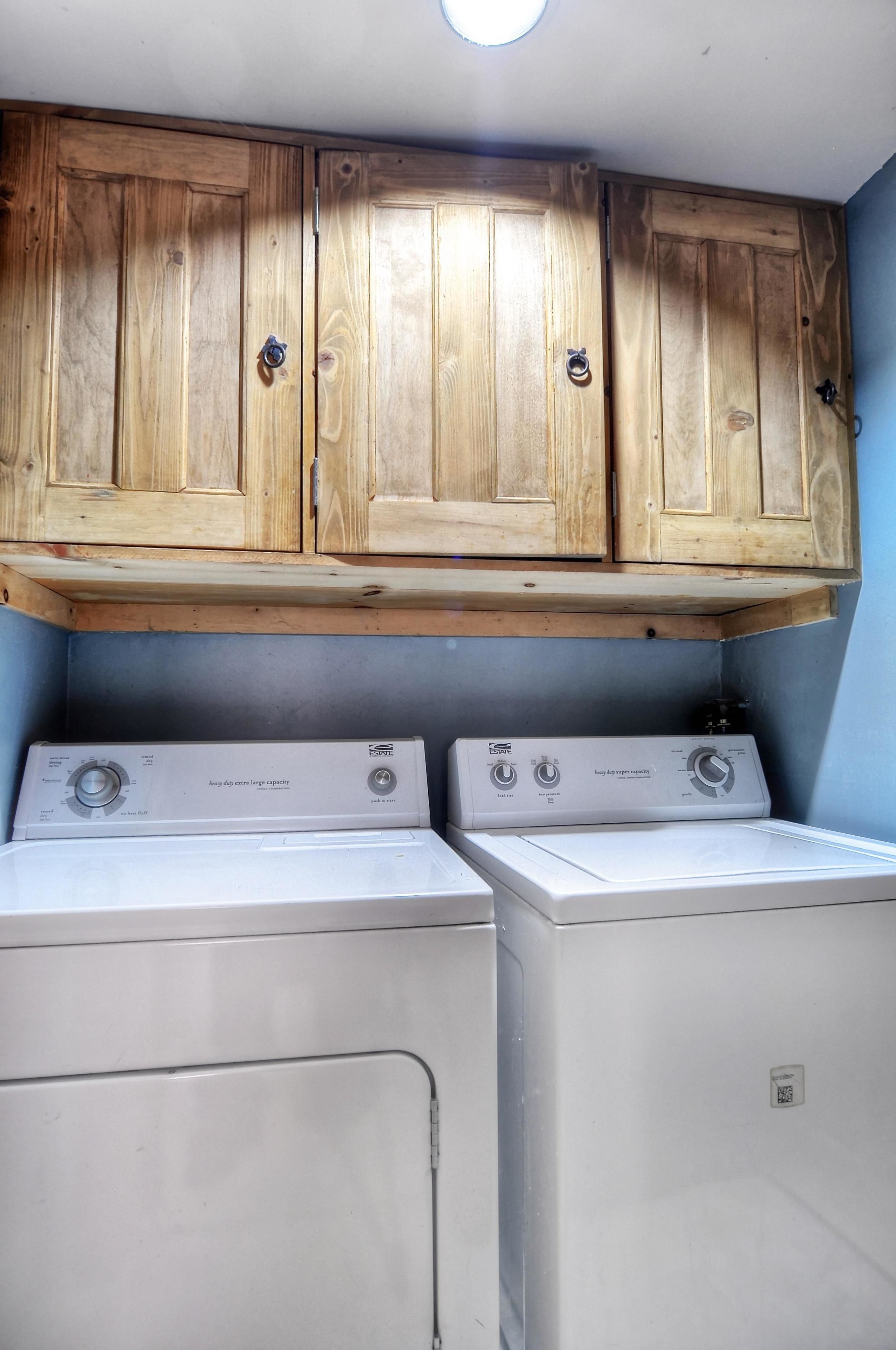 A laundry area with two front-loading washing machines and wooden cabinets above.