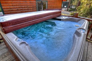 A hot tub with a wooden deck and a wooden cabin in the background.