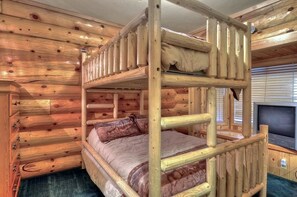 A bunk bed in a log cabin room with a television on the right side.