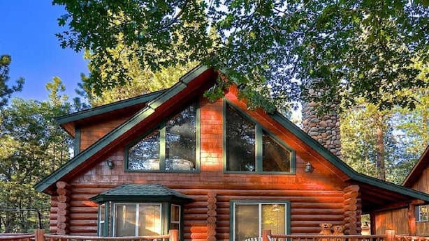 A log cabin with a front porch, large windows, and a stone fireplace.