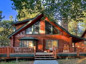 A log cabin with a front porch, large windows, and a stone fireplace.