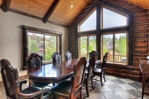 Un salón de conferencias con una gran mesa de madera y sillas, ventanas amplias con vistas al exterior y techo de madera.