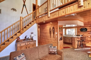 Un interior de madera con una escalera, un sofá, una zona de cocina y un comedor.