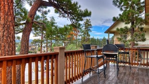 A wooden deck with outdoor furniture, surrounded by trees and a view of a residential area.