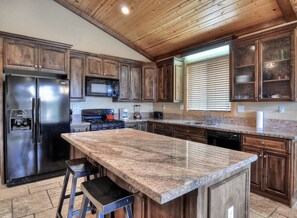 Una cocina con armarios de madera, un refrigerador de acero inoxidable, una encimera de granito y una ventana con persianas.