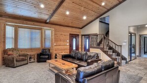 A spacious living room with a wooden ceiling, leather sofas, a coffee table, and a staircase leading to another level.