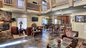 A spacious living area with a stone fireplace, leather furniture, and a high ceiling with wooden beams.