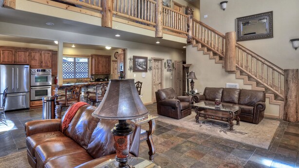A spacious living area with a high ceiling, a wooden staircase, and a kitchen in the background.