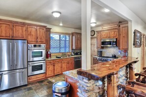 Una cocina con gabinetes de madera, electrodomésticos de acero inoxidable, encimera de granito y una isla de piedra.