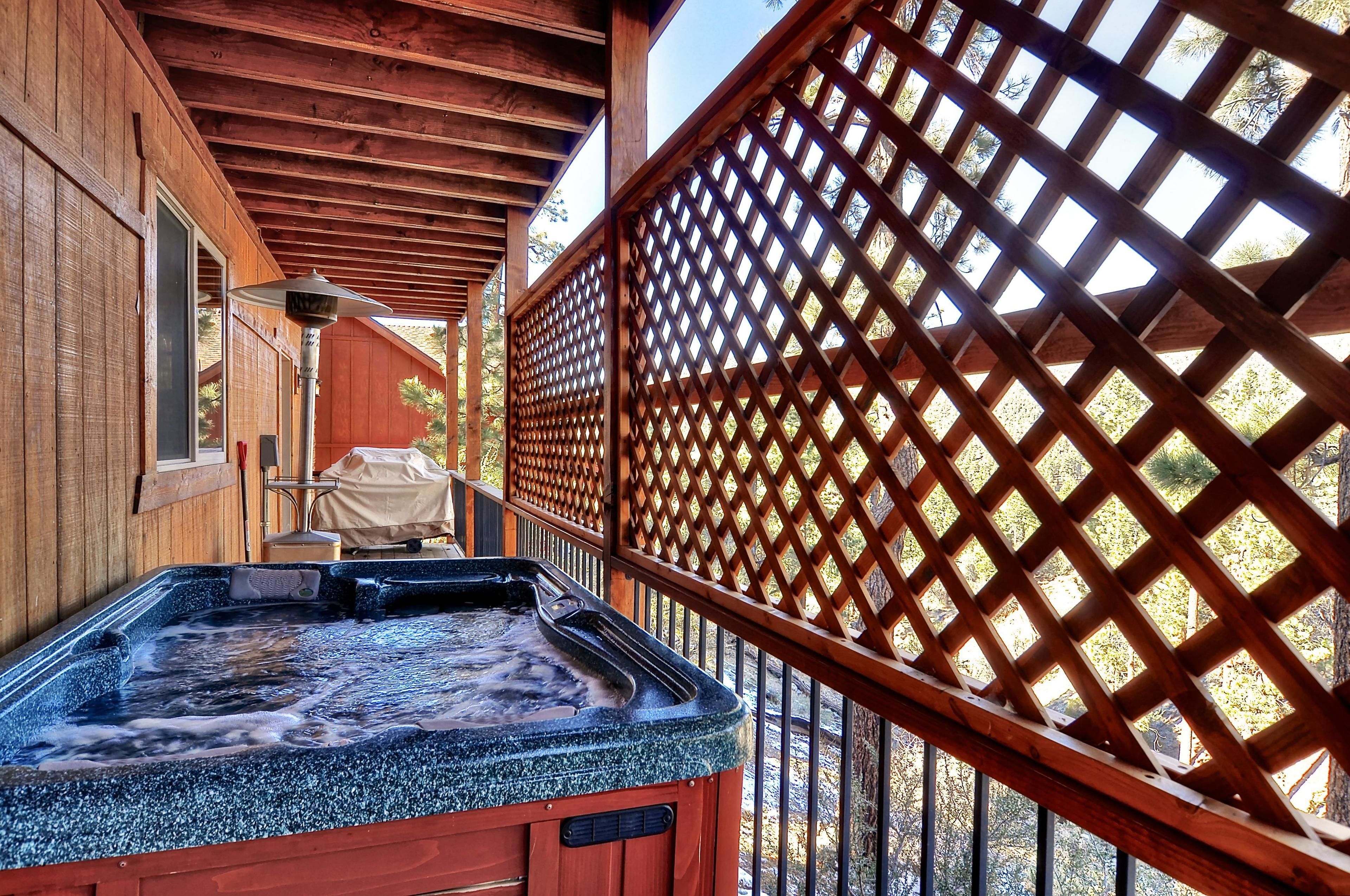 A hot tub area with a wooden deck and lattice screen, surrounded by wooden walls and trees.