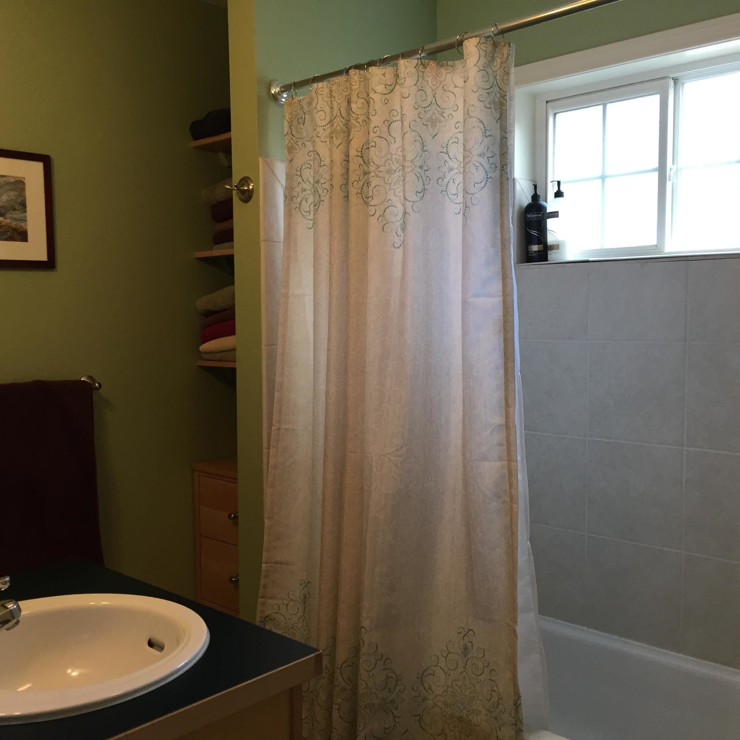 A bathroom with a shower curtain, a sink, and a window.