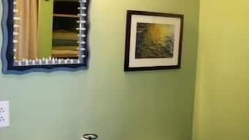 Casa de banho com lavatório branco, sanita, espelho com moldura original e quadro emoldurado na parede.