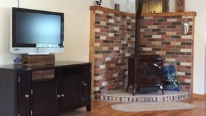 A living room with a television on a cabinet, a brick fireplace, and a wooden floor. - River Lover's 3 Bedroom Holiday Home By Pinon Vacation Rent. (Howard)