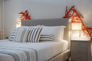 A neatly made bed with striped bedding and a grey headboard, a bedside lamp, and a nightstand with drawers.