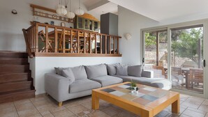 Een moderne woonkamer met een grijze modulaire bank, een houten salontafel en een trap die naar een balkon leidt.