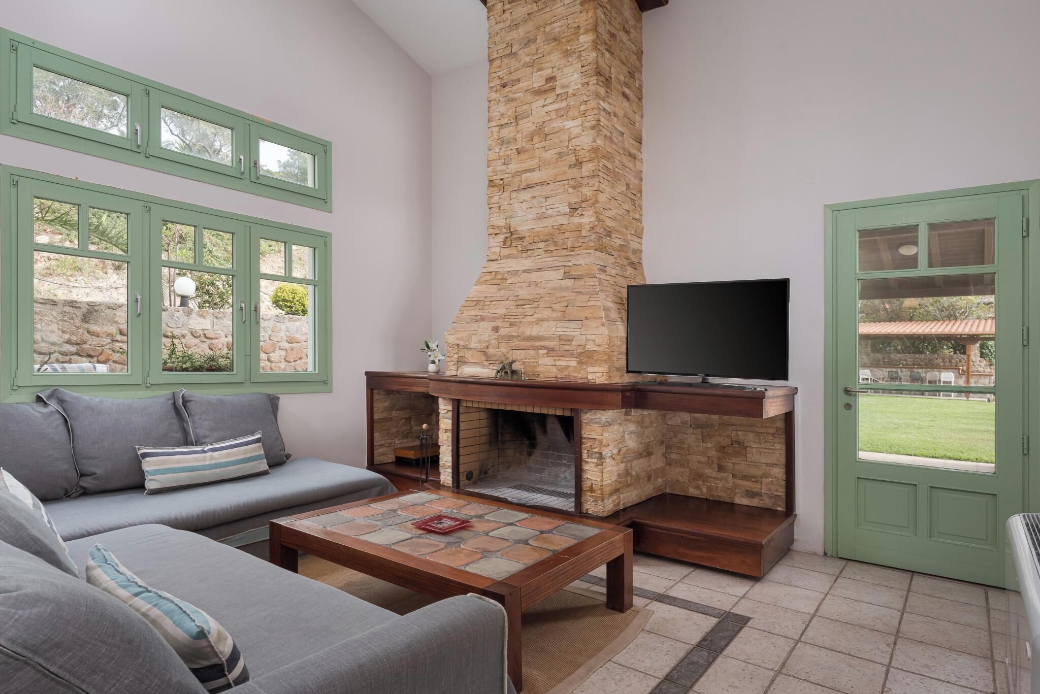 A living room with a stone fireplace, a sofa, a television, and a door leading outside.