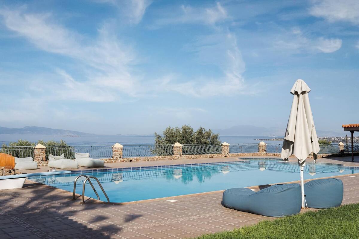 Une piscine avec vue sur la mer, entourée de murs en pierre et d’une clôture en métal.