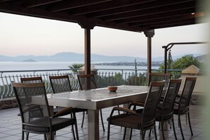 An outdoor patio with a table and chairs, overlooking a body of water and mountains.