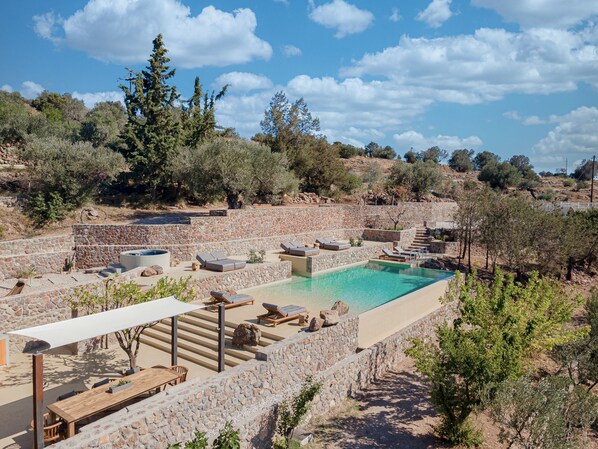 A pool area with stone walls, lounge chairs, and a wooden table.