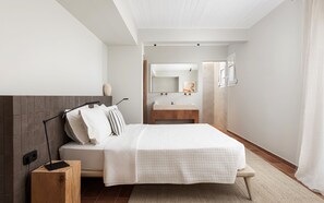 A modern bedroom with a bed, bedside table, and a view of the bathroom. - Aelia & Melitta Villas (Aegina)