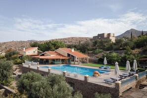 A resort with a swimming pool, outdoor seating, and a view of a hill with a castle-like structure.