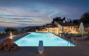 A swimming pool with a stone wall and lounge chairs, surrounded by a stone deck and a view of the sea.