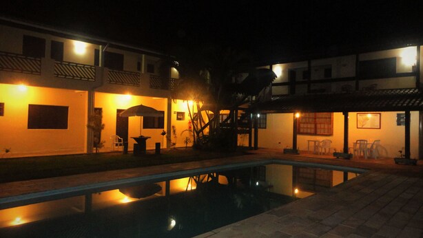 Vista nocturna de un patio de hotel con piscina, mobiliario exterior y una escalera que lleva a un nivel superior.