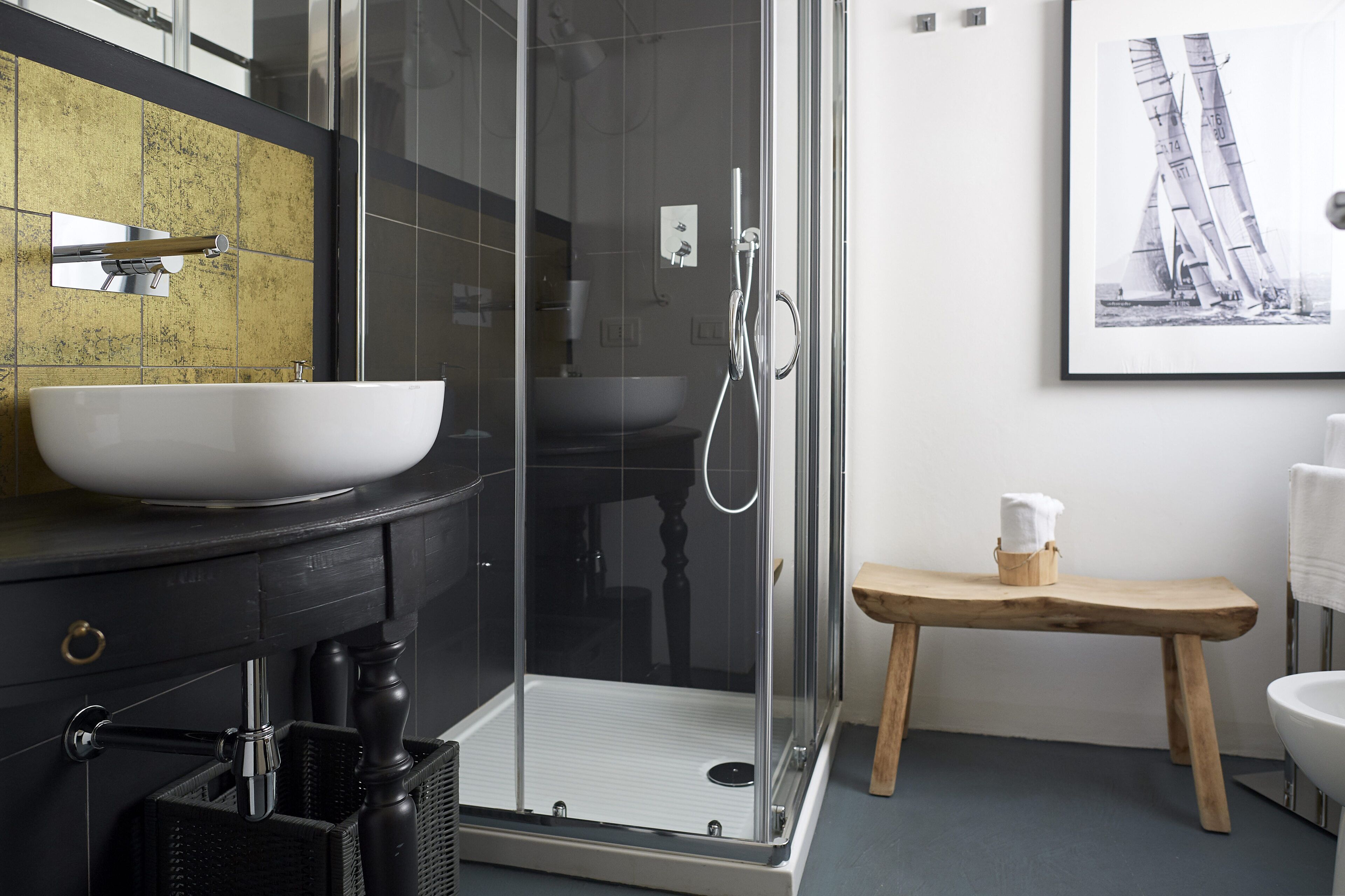A modern bathroom with a glass-enclosed shower, a large white sink, and a wooden bench.