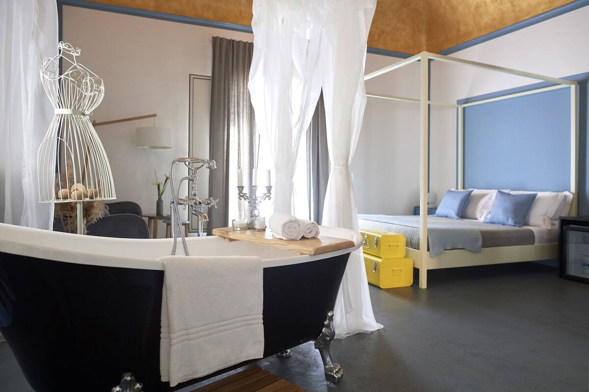 Ein modernes Schlafzimmer mit einer schwarzen Badewanne, einem Himmelbett und einem Nachttisch mit Spiegel und Kerzen.