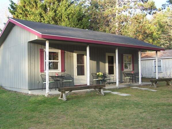 A small, single-story building with a porch, two windows, and a bench.
