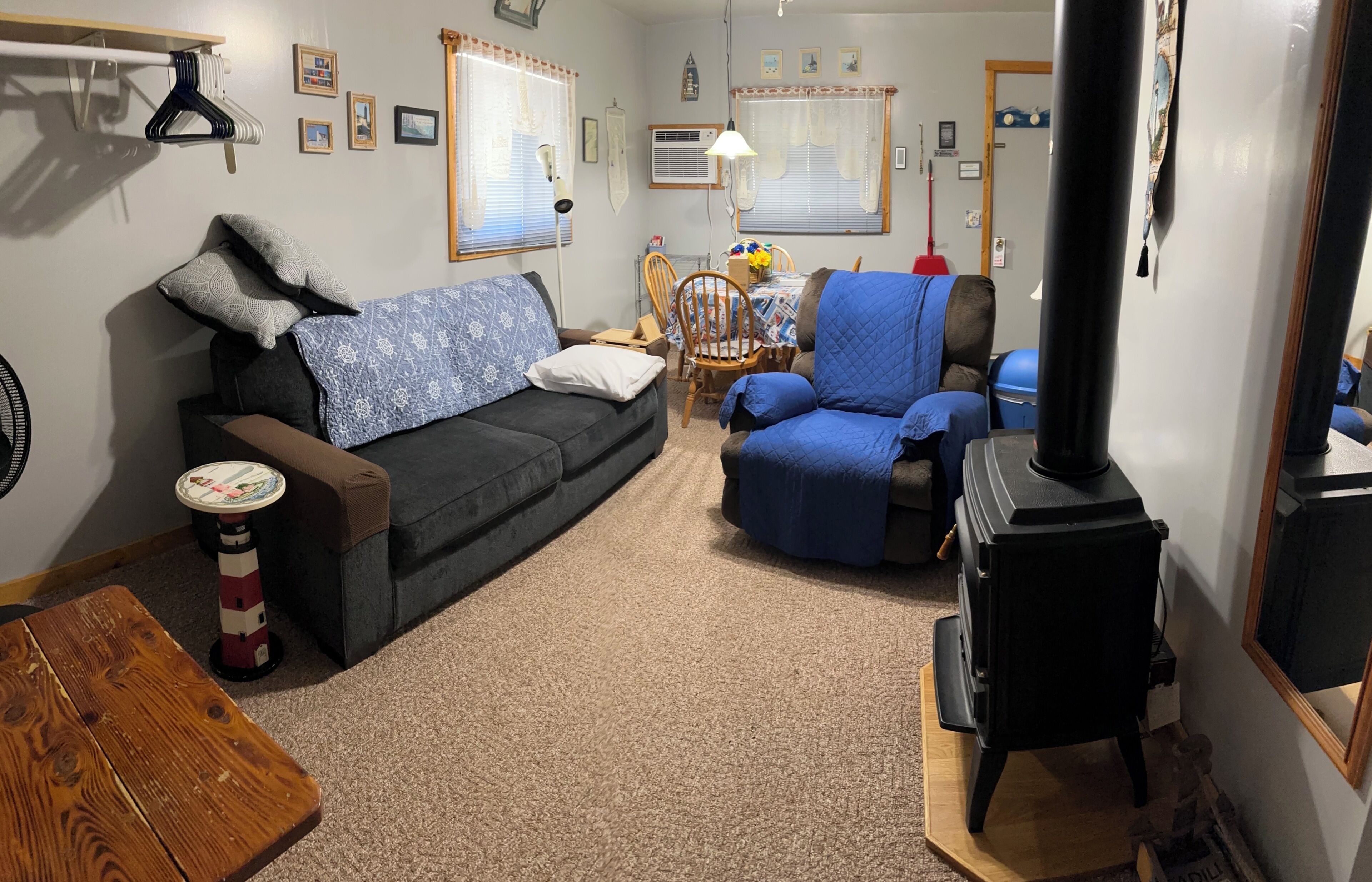 Ein gemütliches Wohnzimmer mit Sofa, Sessel, kleinem Tisch, Ventilator, Lampe, Tischlampe, Heizgerät und einem Fenster mit Vorhängen.