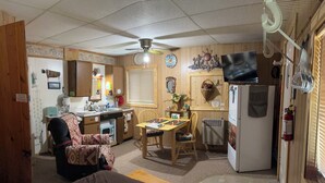 A compact room with a bed, a desk, a chair, a refrigerator, a television, and a ceiling fan.