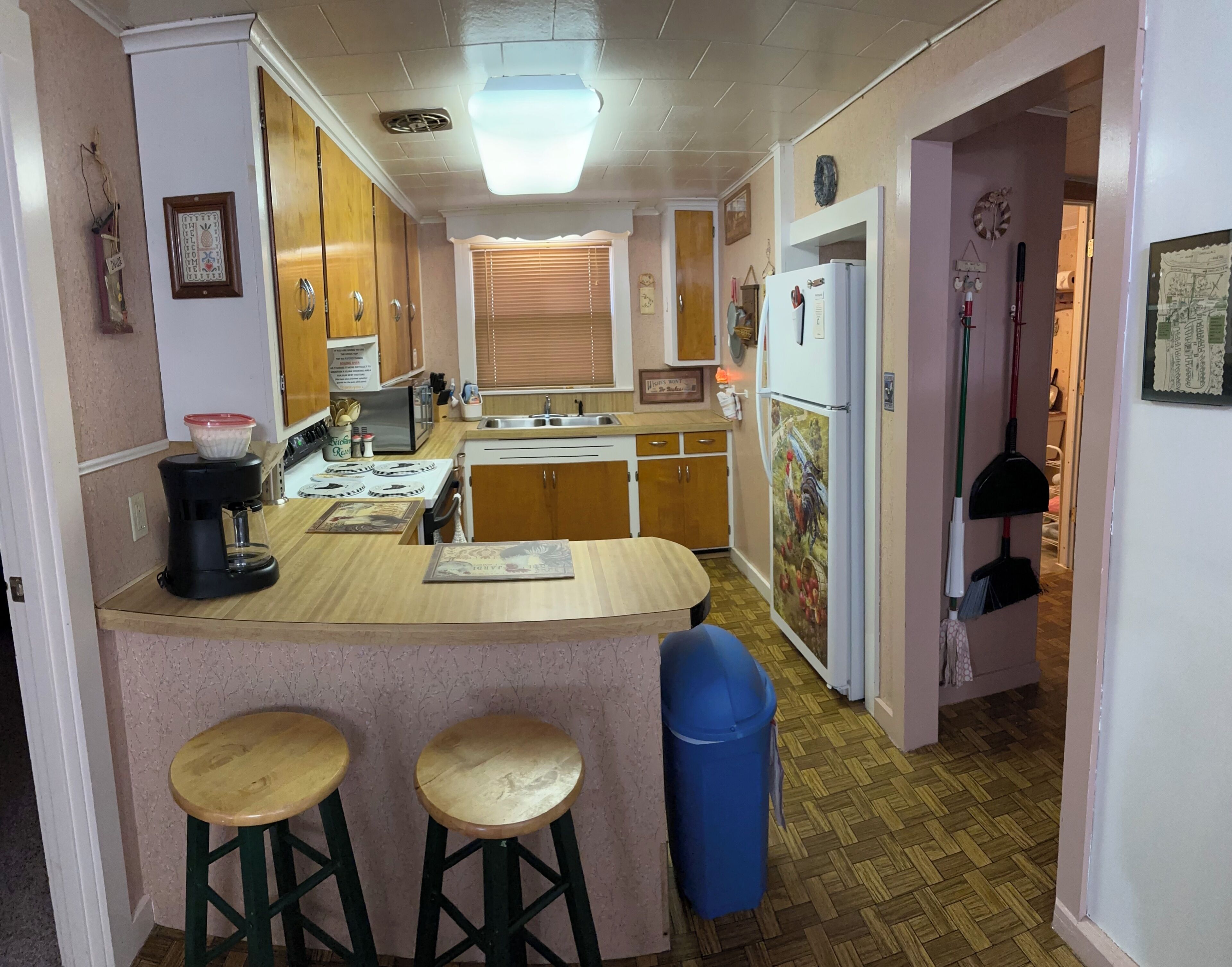 Una cocina compacta con armarios de madera, cafetera, refrigerador con un dibujo de gallo y un cubo de basura azul.