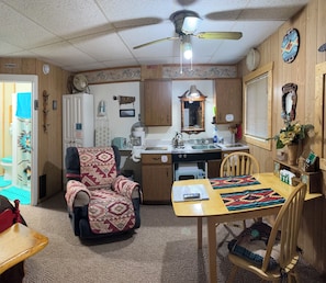 A compact RV interior with a kitchenette, a dining area, a living space, and a ceiling fan.