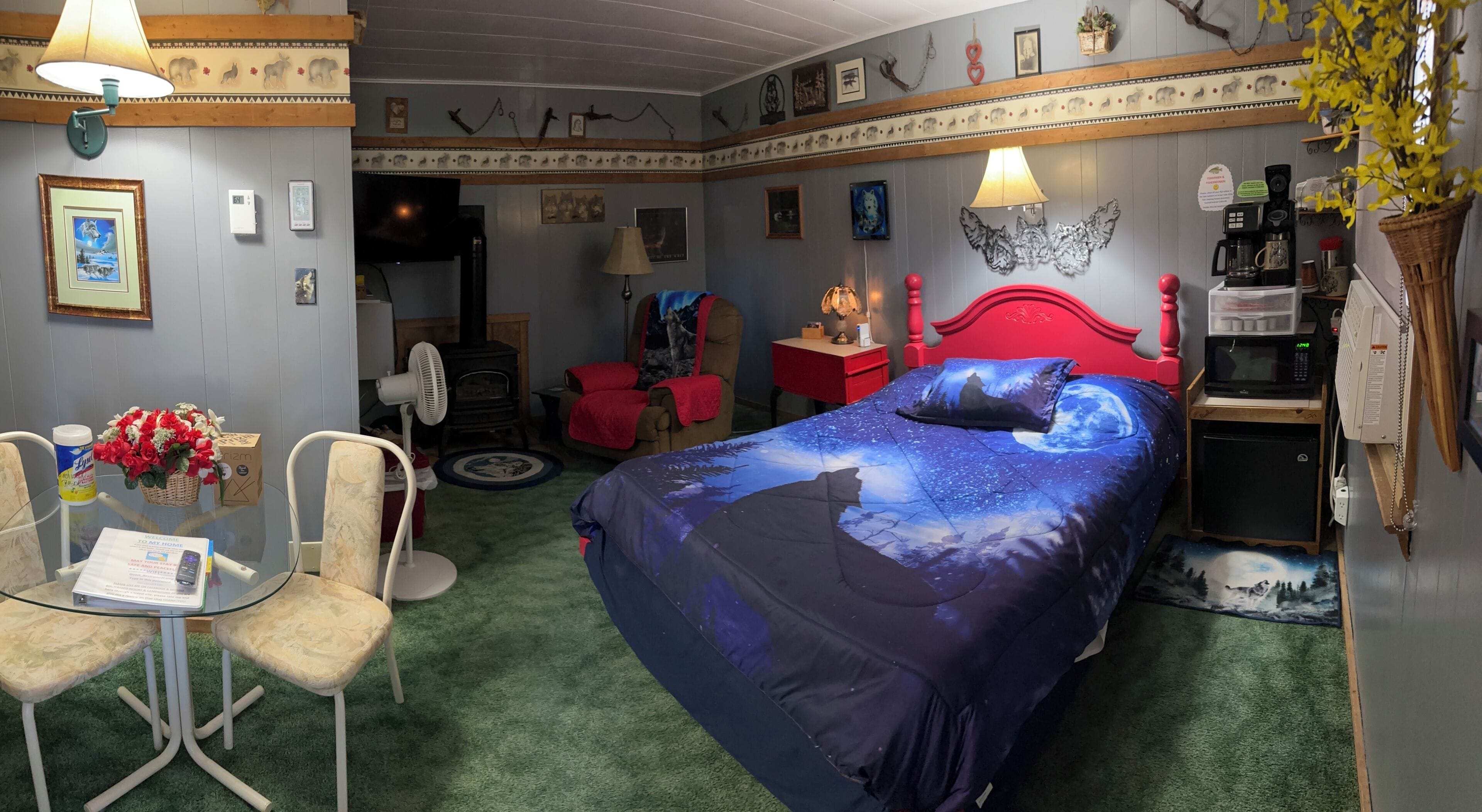 A room with a bed, a desk, chairs, a lamp, a fan, a microwave, and a small refrigerator.
