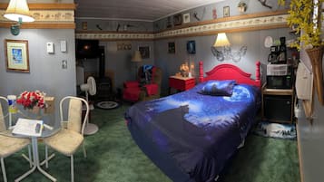 A room with a bed, a desk, chairs, a lamp, a fan, a microwave, and a small refrigerator.