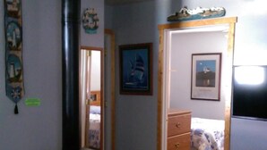 A cozy living room with a wood-burning stove, a bed with a blue and white striped blanket, and a dresser.