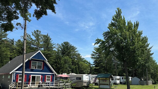 A blue house with a porch, RVs, and a small shed in a grassy area with trees.