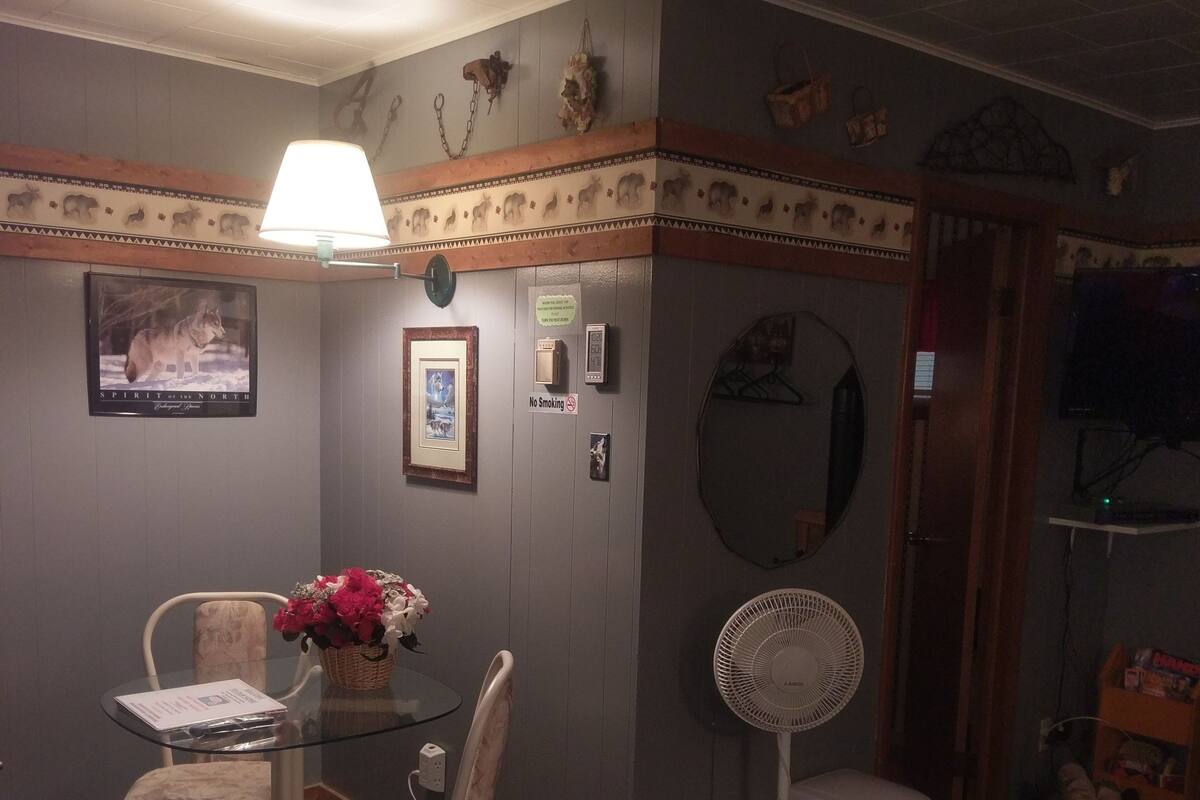 Une chambre d’hôtel avec un lit, une table et des chaises, un ventilateur, une télévision et un mur orné de tableaux et d’un panneau « Il est interdit de fumer ».