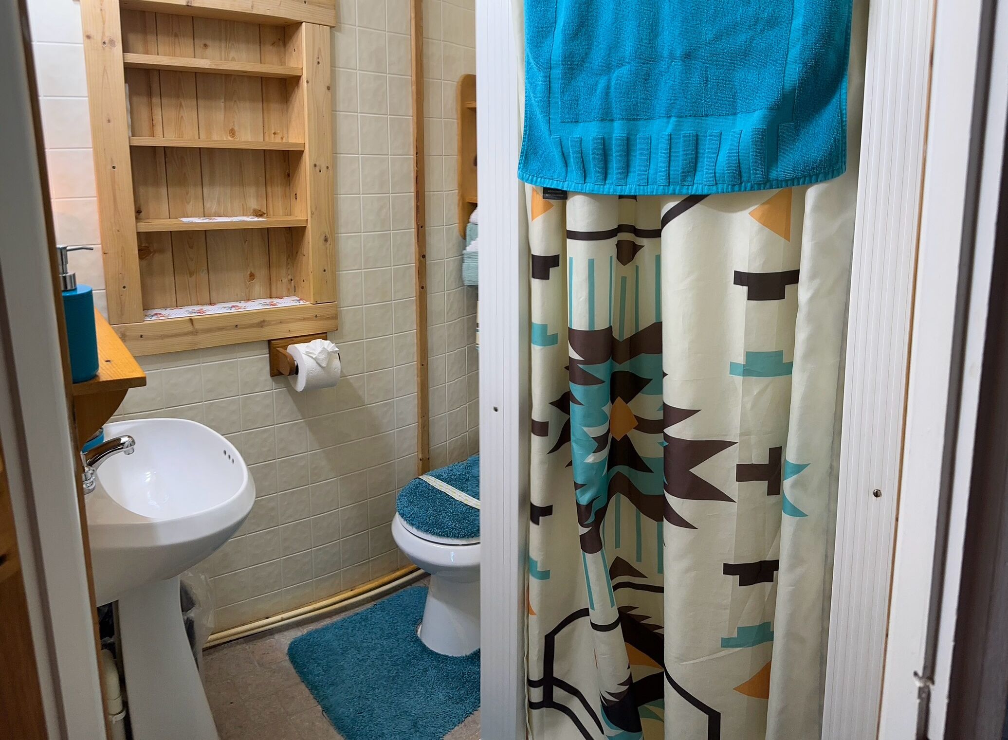 A bathroom with a wooden shelf, toilet, and a blue mat.