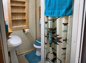 A bathroom with a wooden shelf, toilet, and a blue mat.