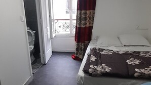 A bedroom with a bed, a small table, and a view of the outside. - Hôtel des Andelys (Paris)